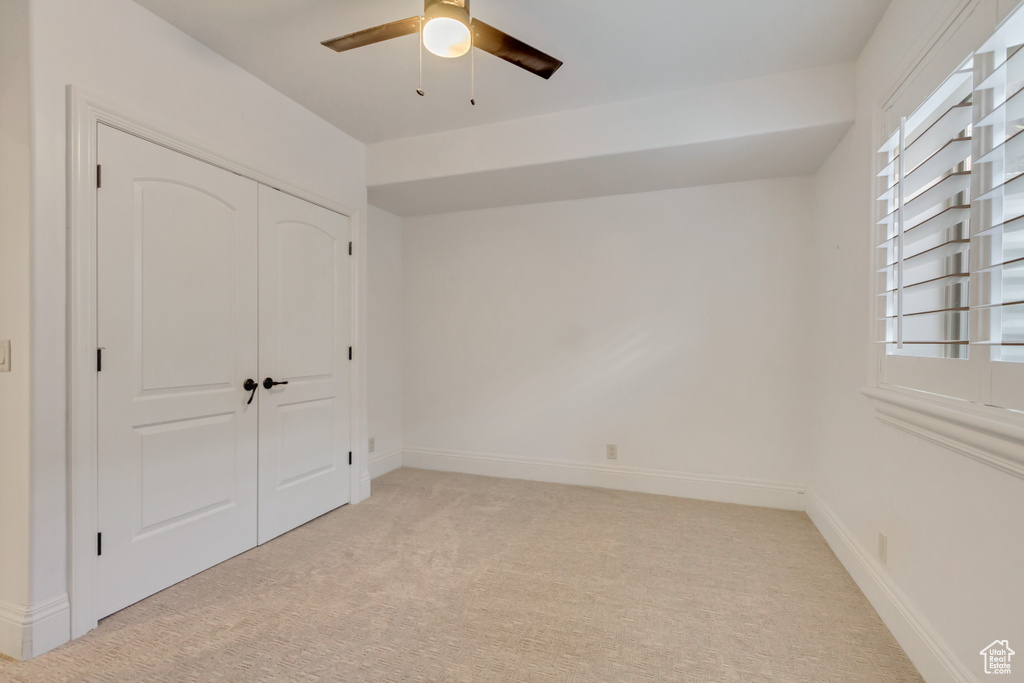 Unfurnished bedroom featuring light colored carpet, a closet, and ceiling fan