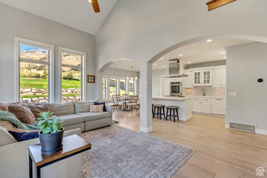 Living room featuring light hardwood / wood-style floors, high vaulted ceiling, sink, and ceiling fan with notable chandelier