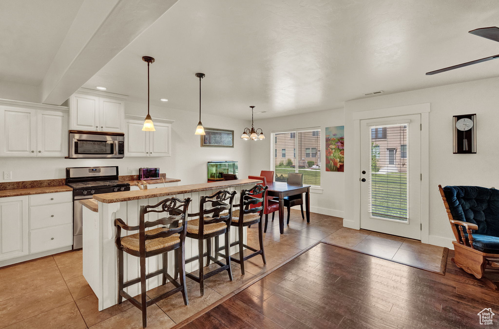 Kitchen featuring white cabinetry, hanging light fixtures, appliances with stainless steel finishes, a kitchen bar, and light tile floors