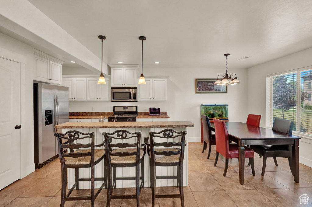 Kitchen featuring decorative light fixtures, white cabinetry, light tile floors, and stainless steel appliances