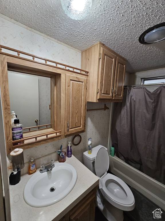 Full bathroom featuring shower / bath combo, a textured ceiling, oversized vanity, and toilet