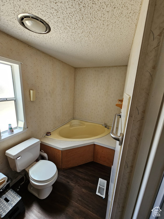 Bathroom with a bath to relax in, hardwood / wood-style floors, toilet, and a textured ceiling