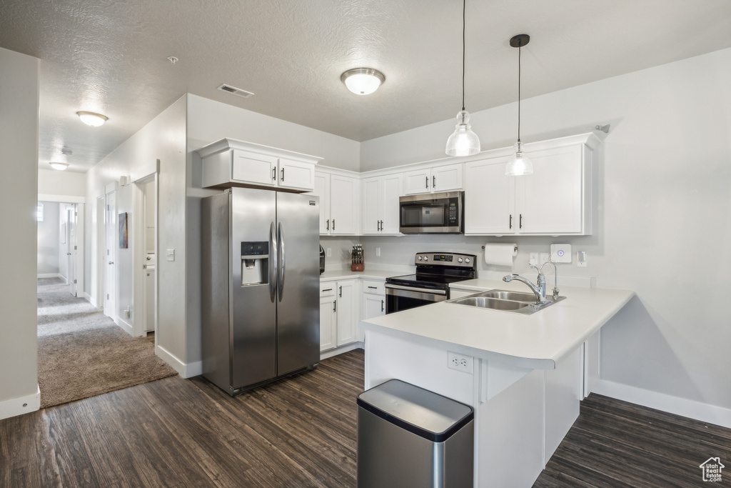 Kitchen with white cabinetry, stainless steel appliances, kitchen peninsula, sink, and dark carpet