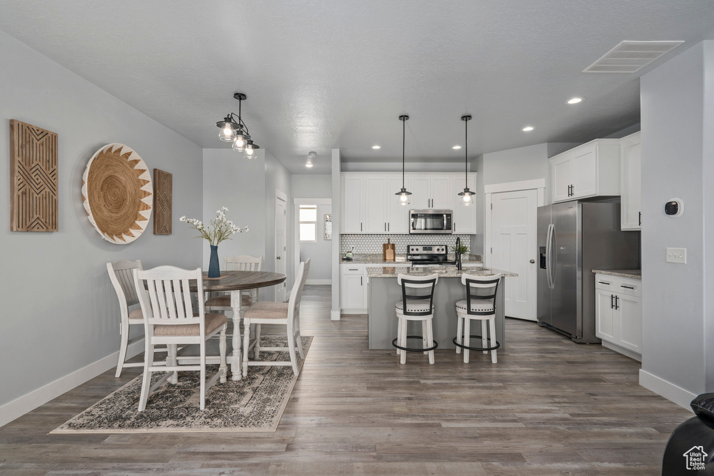 Kitchen with dark wood-type flooring, a center island with sink, stainless steel appliances, decorative light fixtures, and a kitchen bar