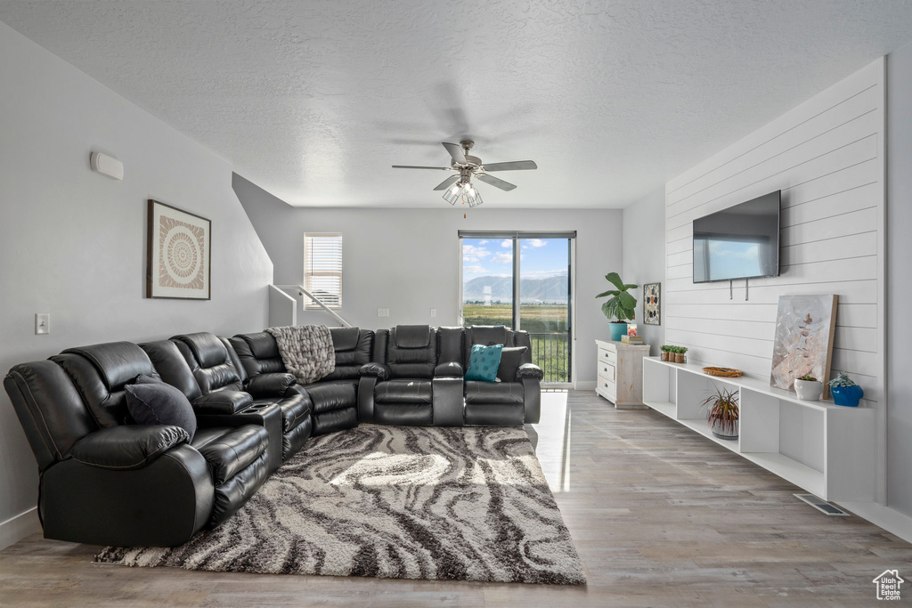 Living room with wood walls, ceiling fan, a textured ceiling, and light wood-type flooring