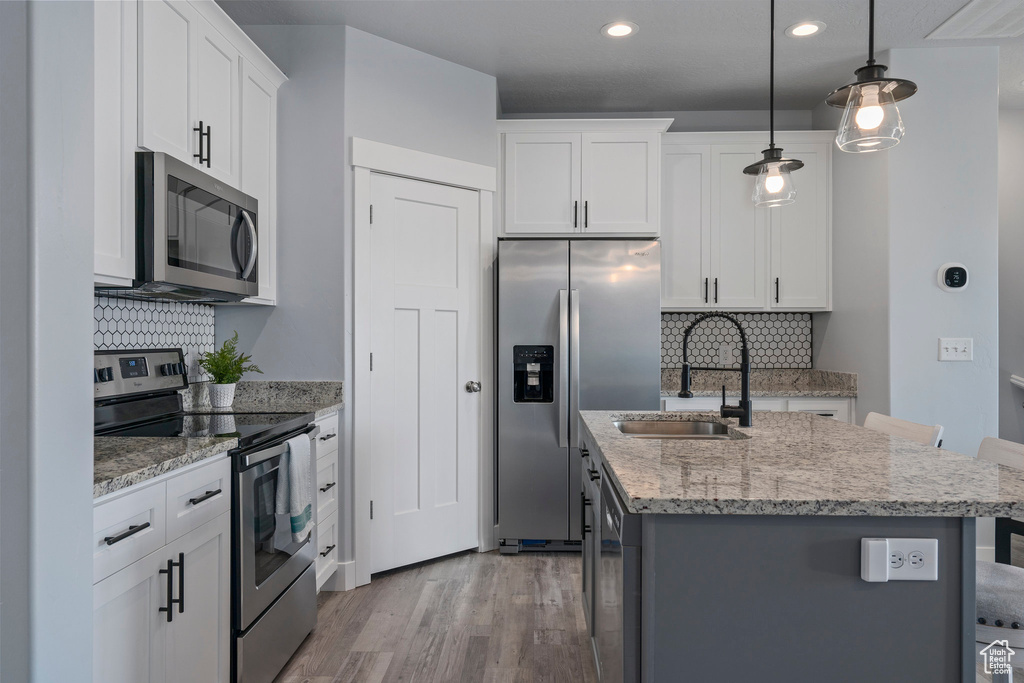 Kitchen featuring hardwood / wood-style floors, stainless steel appliances, pendant lighting, backsplash, and a kitchen island with sink