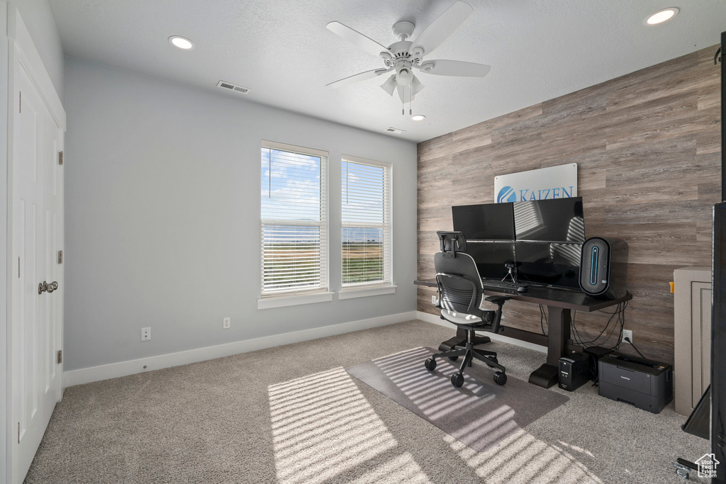 Home office featuring carpet flooring, wooden walls, and ceiling fan