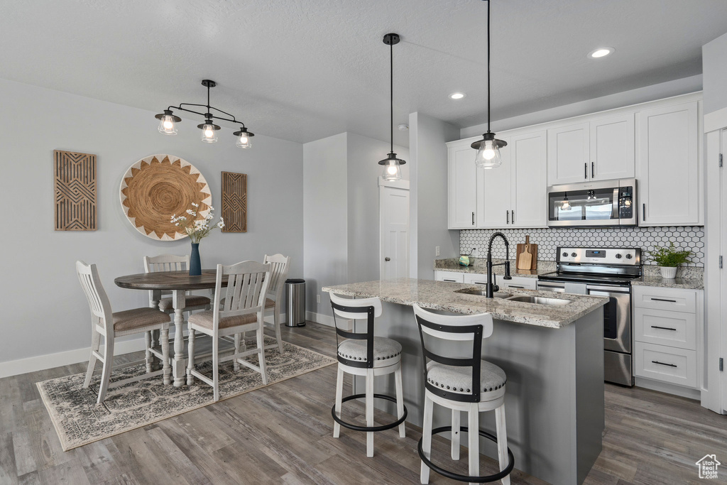 Kitchen featuring hanging light fixtures, hardwood / wood-style floors, white cabinetry, and appliances with stainless steel finishes