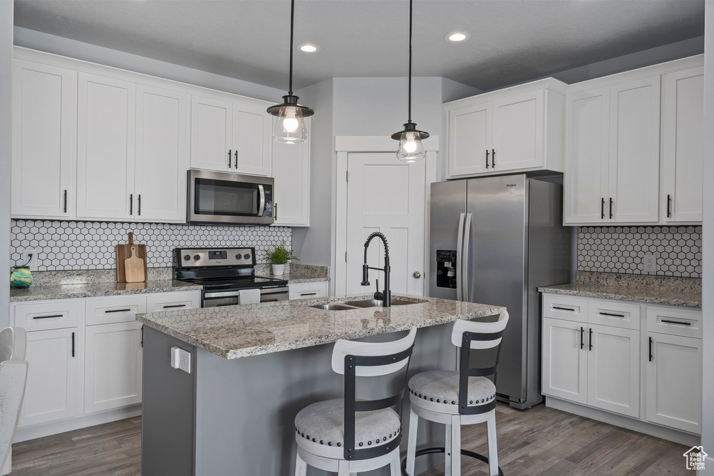 Kitchen featuring stainless steel appliances, decorative light fixtures, backsplash, sink, and hardwood / wood-style flooring