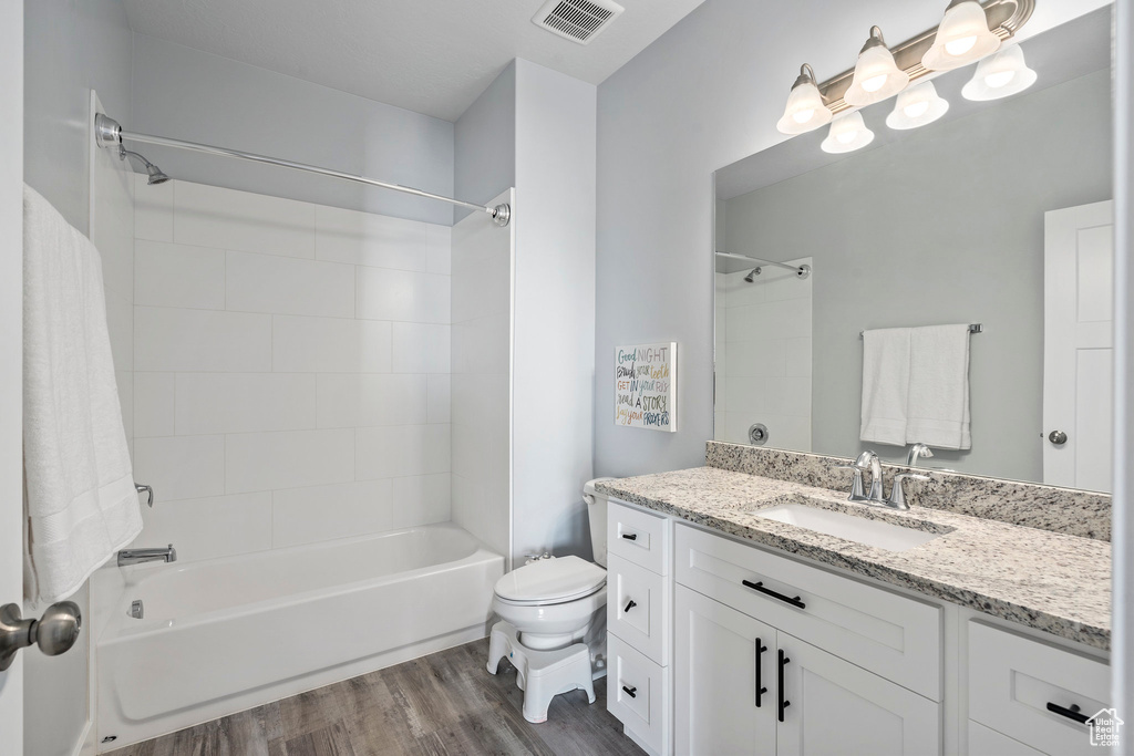 Full bathroom featuring tiled shower / bath, hardwood / wood-style flooring, toilet, and vanity