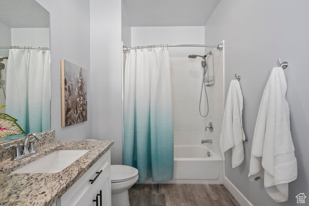 Full bathroom with shower / bathtub combination with curtain, a textured ceiling, hardwood / wood-style flooring, large vanity, and toilet