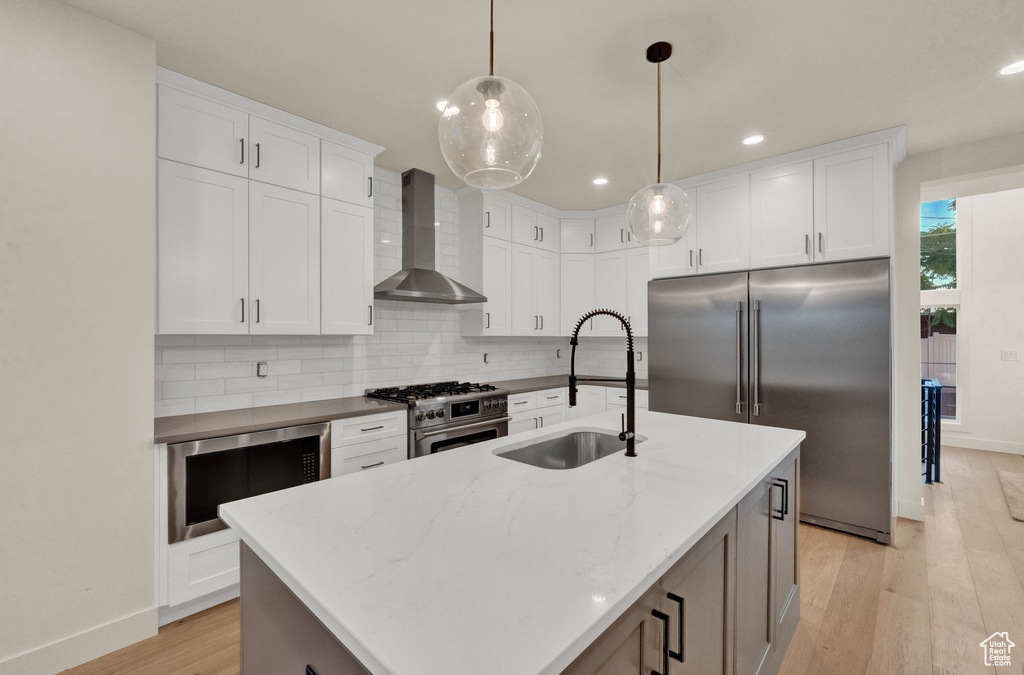 Kitchen featuring light hardwood / wood-style flooring, a center island with sink, backsplash, high quality appliances, and wall chimney exhaust hood