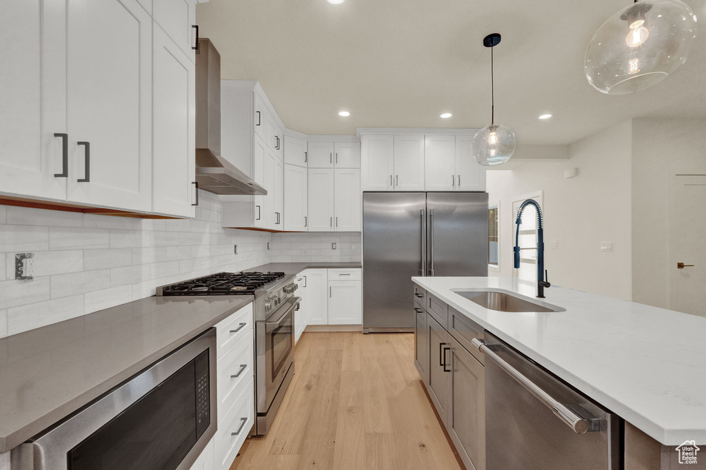 Kitchen with light wood-type flooring, wall chimney exhaust hood, backsplash, built in appliances, and sink