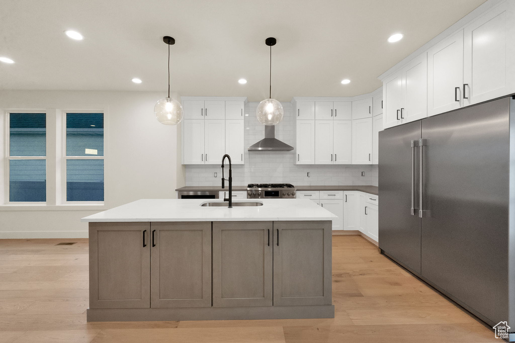 Kitchen featuring white cabinetry, light hardwood / wood-style flooring, a kitchen island with sink, backsplash, and built in fridge