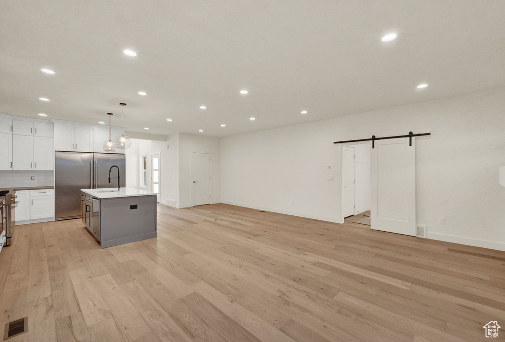 Kitchen with light wood-type flooring, a center island with sink, white cabinets, pendant lighting, and a barn door