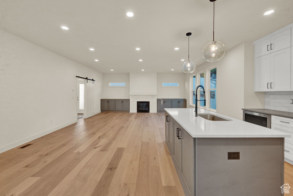 Kitchen featuring light hardwood / wood-style floors, white cabinetry, an island with sink, a barn door, and sink