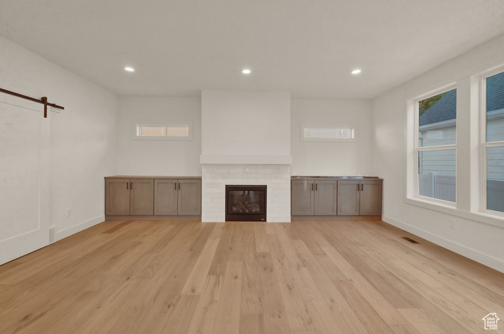 Unfurnished living room with a barn door, light hardwood / wood-style floors, and a brick fireplace