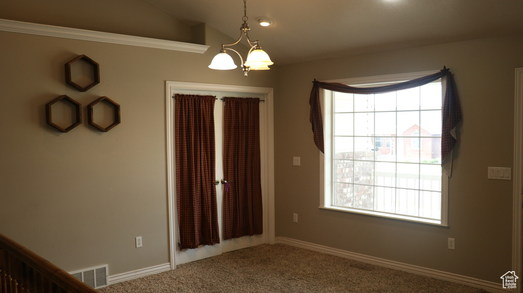 Empty room featuring a healthy amount of sunlight, carpet, vaulted ceiling, and an inviting chandelier