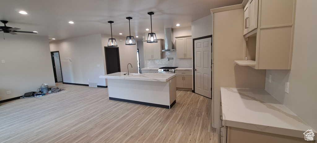 Kitchen featuring light hardwood / wood-style floors, backsplash, hanging light fixtures, ceiling fan, and wall chimney exhaust hood