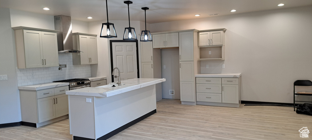 Kitchen with an island with sink, gas stove, wall chimney exhaust hood, and light hardwood / wood-style floors