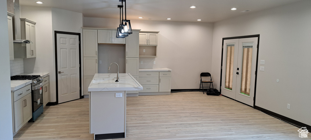 Kitchen with light hardwood / wood-style flooring, stainless steel range with gas stovetop, pendant lighting, backsplash, and a center island