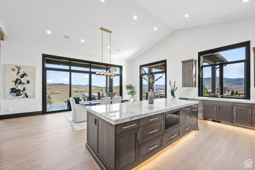 Kitchen featuring light stone counters, hanging light fixtures, stainless steel microwave, a center island, and light wood-type flooring