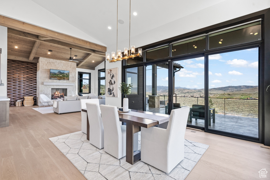 Dining room with light hardwood / wood-style floors, a fireplace, ceiling fan with notable chandelier, wooden ceiling, and high vaulted ceiling