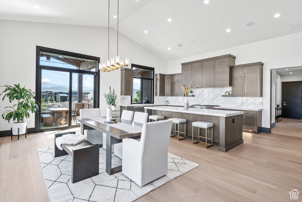 Dining space with high vaulted ceiling, light hardwood / wood-style flooring, and a chandelier