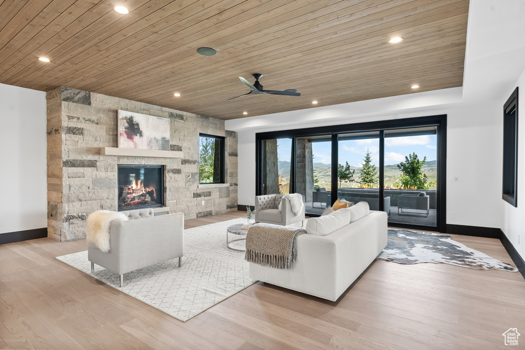 Living room featuring tile walls, ceiling fan, wooden ceiling, a stone fireplace, and light wood-type flooring