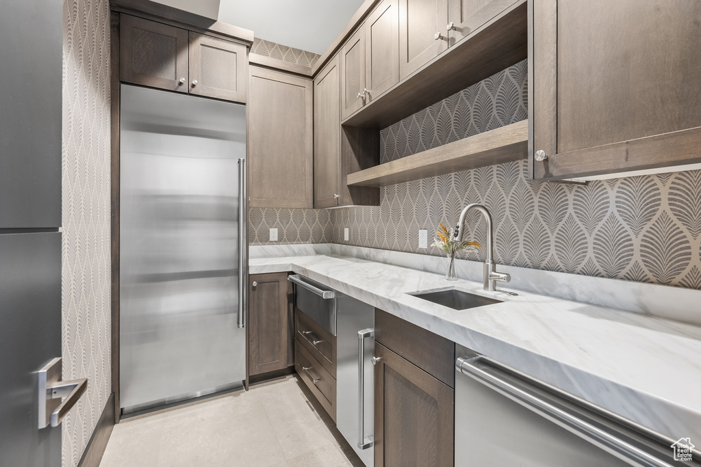 Kitchen featuring stainless steel refrigerator, backsplash, light stone countertops, sink, and stainless steel built in fridge