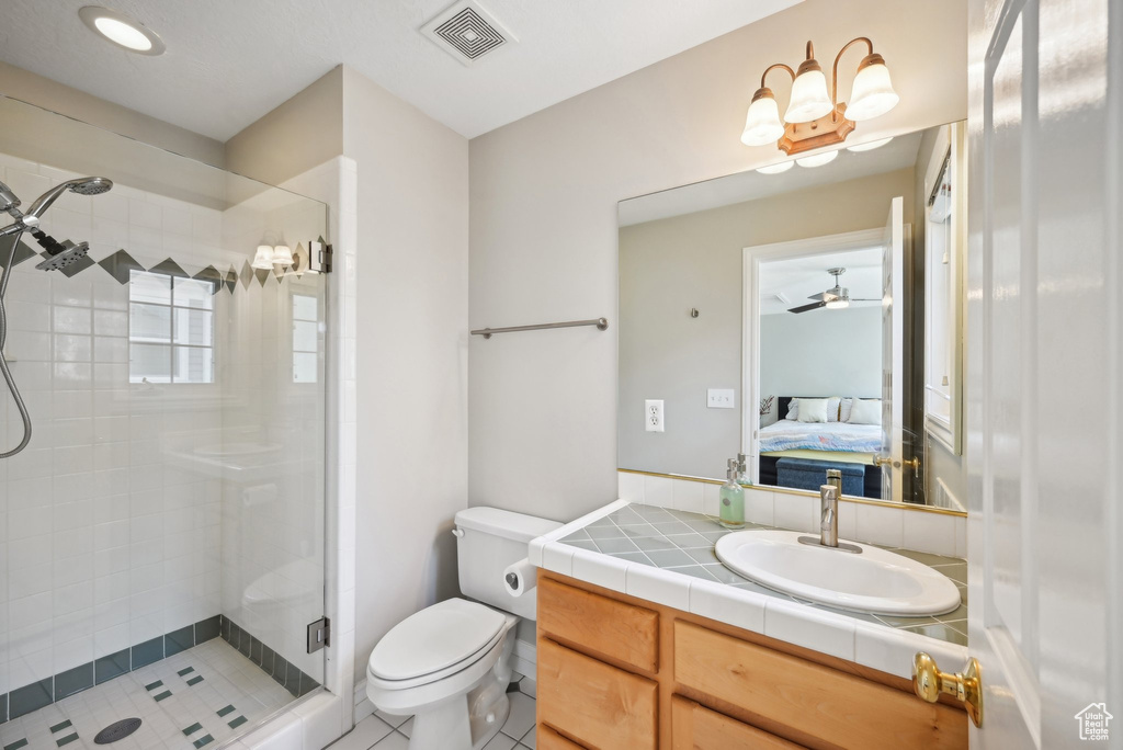 Bathroom featuring vanity with extensive cabinet space, ceiling fan, toilet, tile floors, and a shower with door