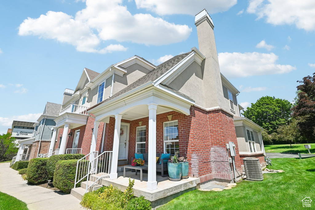 View of front of home with covered porch, a front yard, and central AC