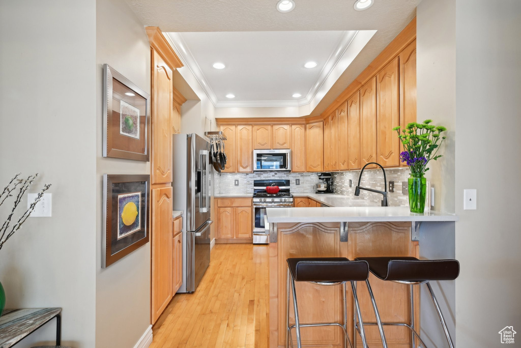 Kitchen with light hardwood / wood-style floors, kitchen peninsula, tasteful backsplash, ornamental molding, and appliances with stainless steel finishes