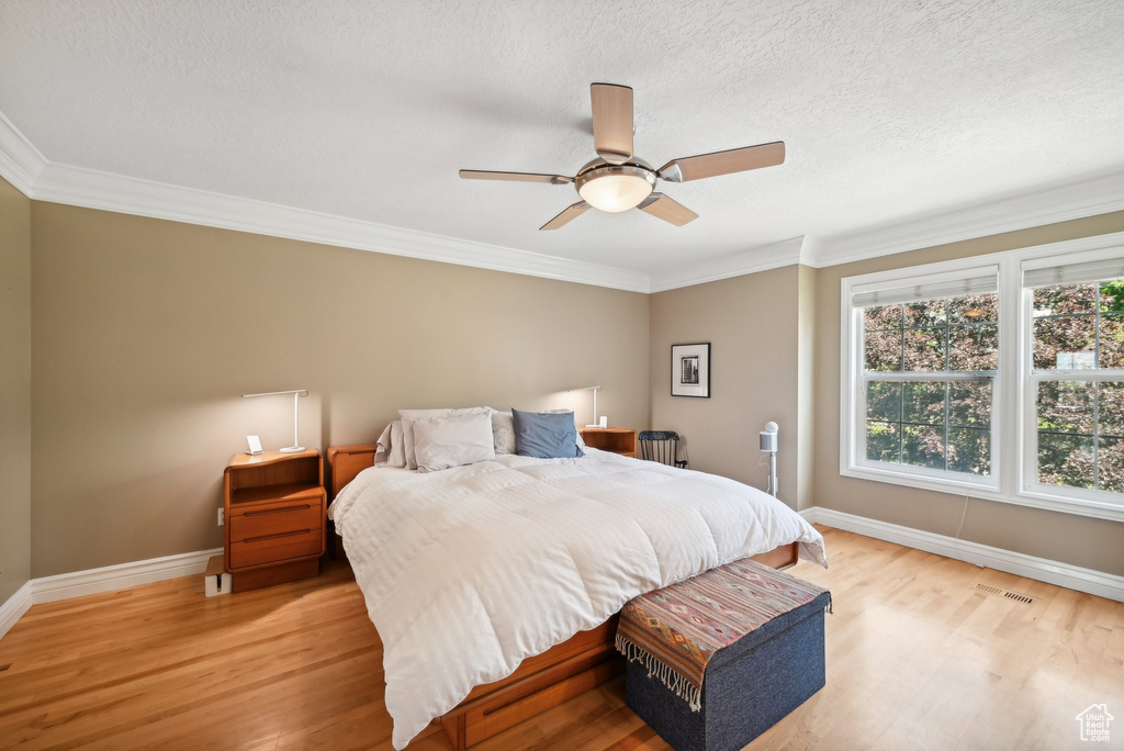 Bedroom featuring crown molding, a textured ceiling, ceiling fan, and light hardwood / wood-style flooring