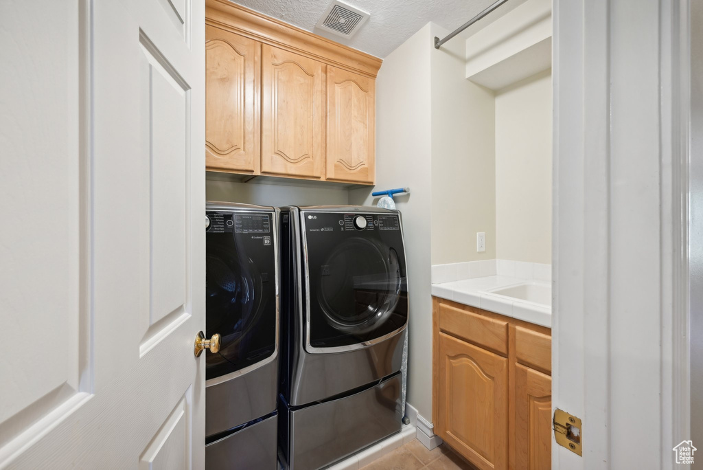 Laundry room with washer and dryer, a textured ceiling, cabinets, and light tile floors