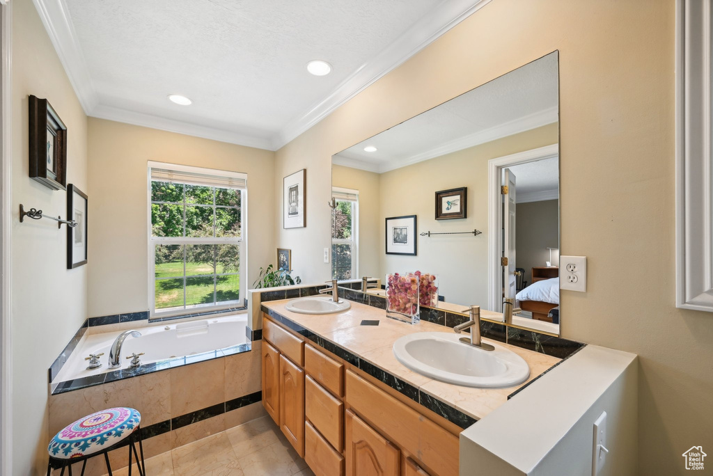 Bathroom featuring tiled bath, ornamental molding, double sink, and oversized vanity