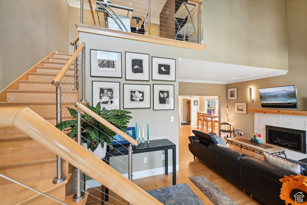 Living room with a premium fireplace, a towering ceiling, crown molding, and wood-type flooring