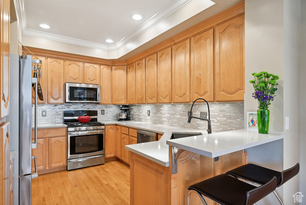 Kitchen featuring kitchen peninsula, stainless steel appliances, light wood-type flooring, backsplash, and a kitchen bar