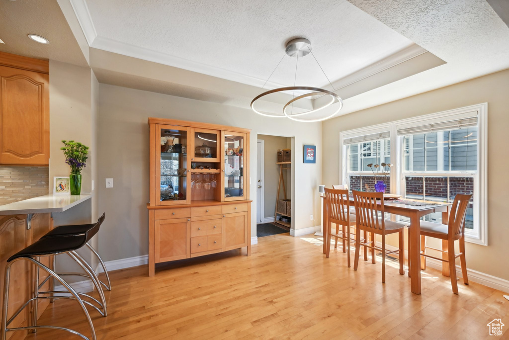 Dining area with light hardwood / wood-style floors, a textured ceiling, a chandelier, and a raised ceiling