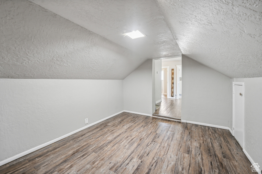 Additional living space with a textured ceiling, vaulted ceiling, and hardwood / wood-style floors