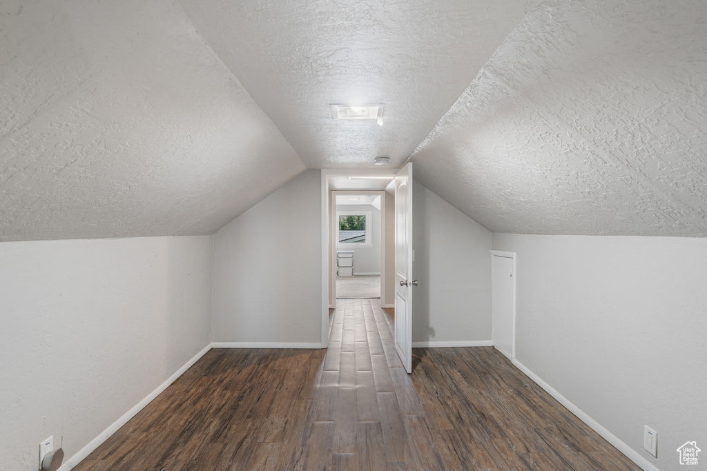 Additional living space with vaulted ceiling, a textured ceiling, and dark wood-type flooring