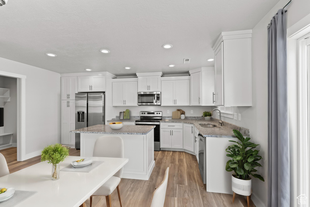 Kitchen featuring light wood-type flooring, a kitchen island, sink, light stone countertops, and appliances with stainless steel finishes