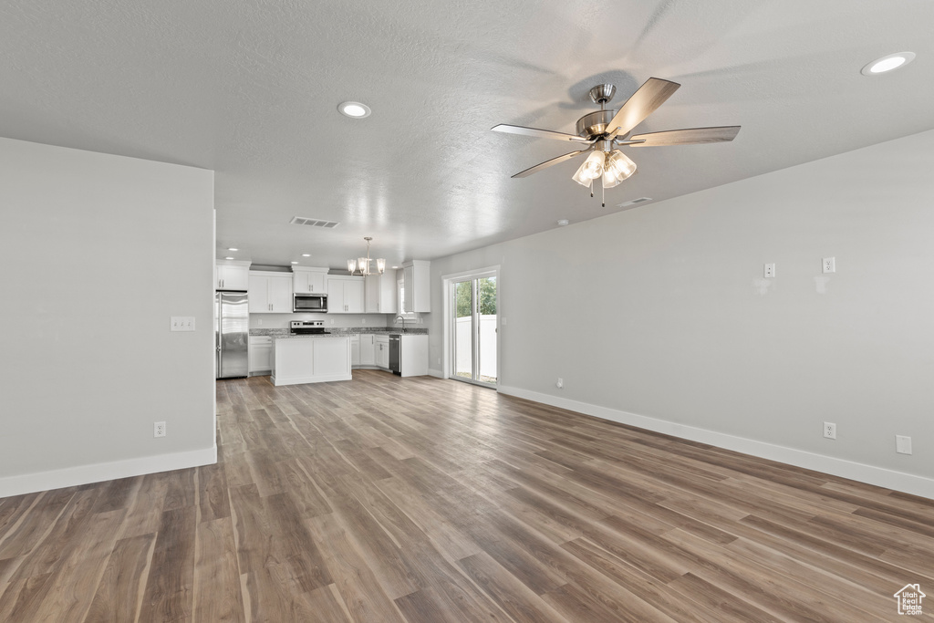 Unfurnished living room featuring a textured ceiling, sink, ceiling fan with notable chandelier, and wood-type flooring