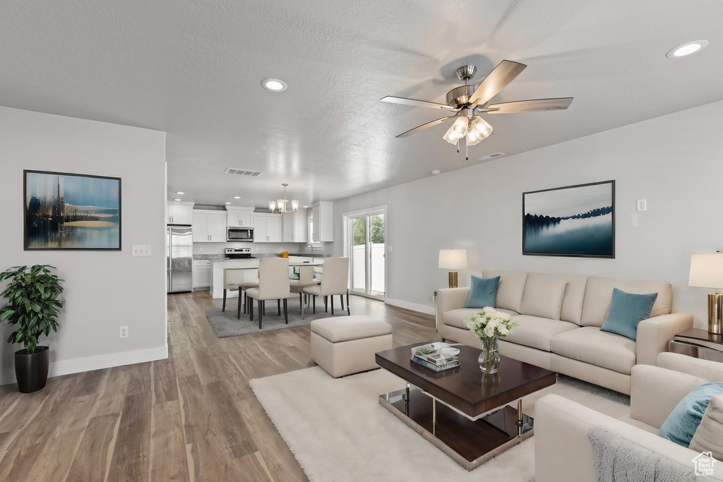 Living room featuring ceiling fan with notable chandelier, light hardwood / wood-style floors, and a textured ceiling