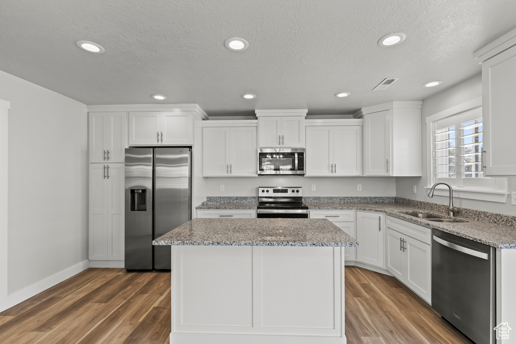 Kitchen with appliances with stainless steel finishes, hardwood / wood-style flooring, sink, and white cabinets