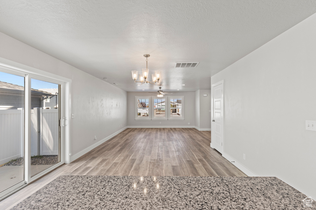 Unfurnished dining area with a textured ceiling, ceiling fan with notable chandelier, and hardwood / wood-style flooring