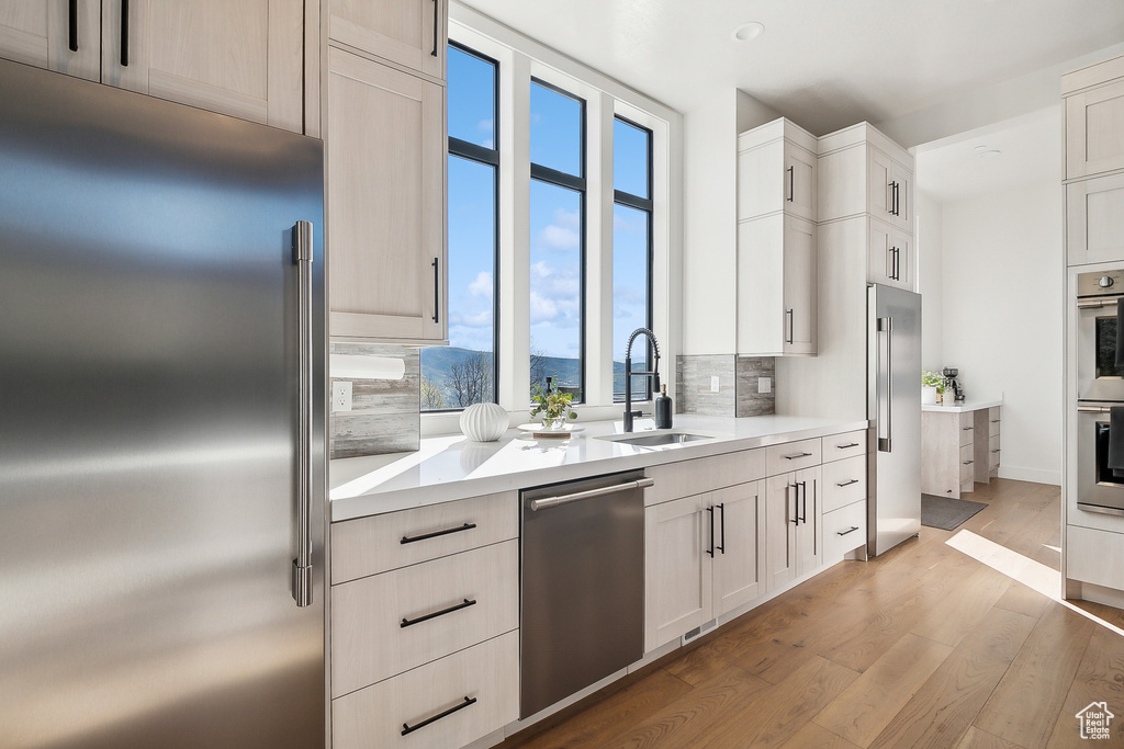 Kitchen featuring stainless steel appliances, a sink, backsplash, light wood finished floors, and light countertops