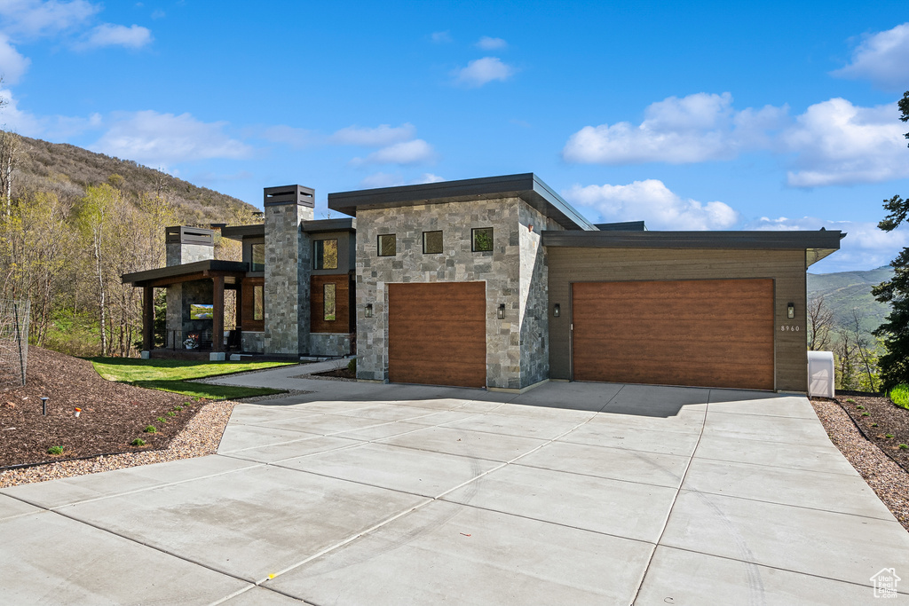 Contemporary house featuring concrete driveway, a mountain view, a garage, and stone siding