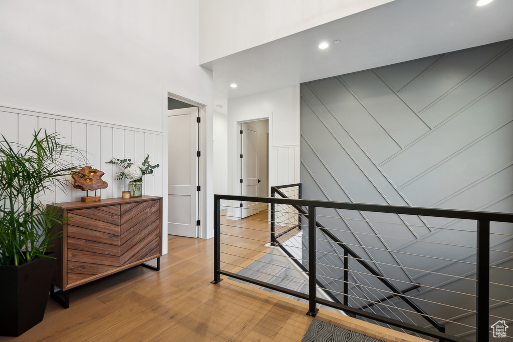 Corridor featuring a decorative wall, an upstairs landing, wood finished floors, a towering ceiling, and a wainscoted wall