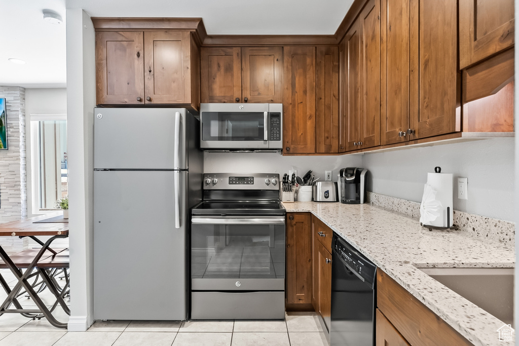 Kitchen with light stone counters, light tile flooring, and appliances with stainless steel finishes